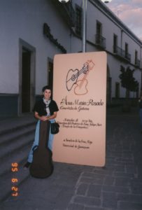 AMR Standing In Front Of Large Poster On The Street With Her Guitar